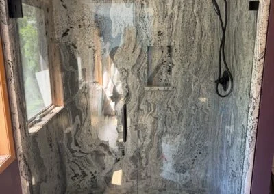 Frameless glass shower with matte black hardware and marble-look walls