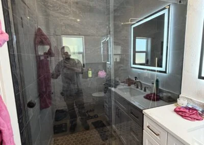 Frameless sliding shower door with black hardware beside a lit mirror